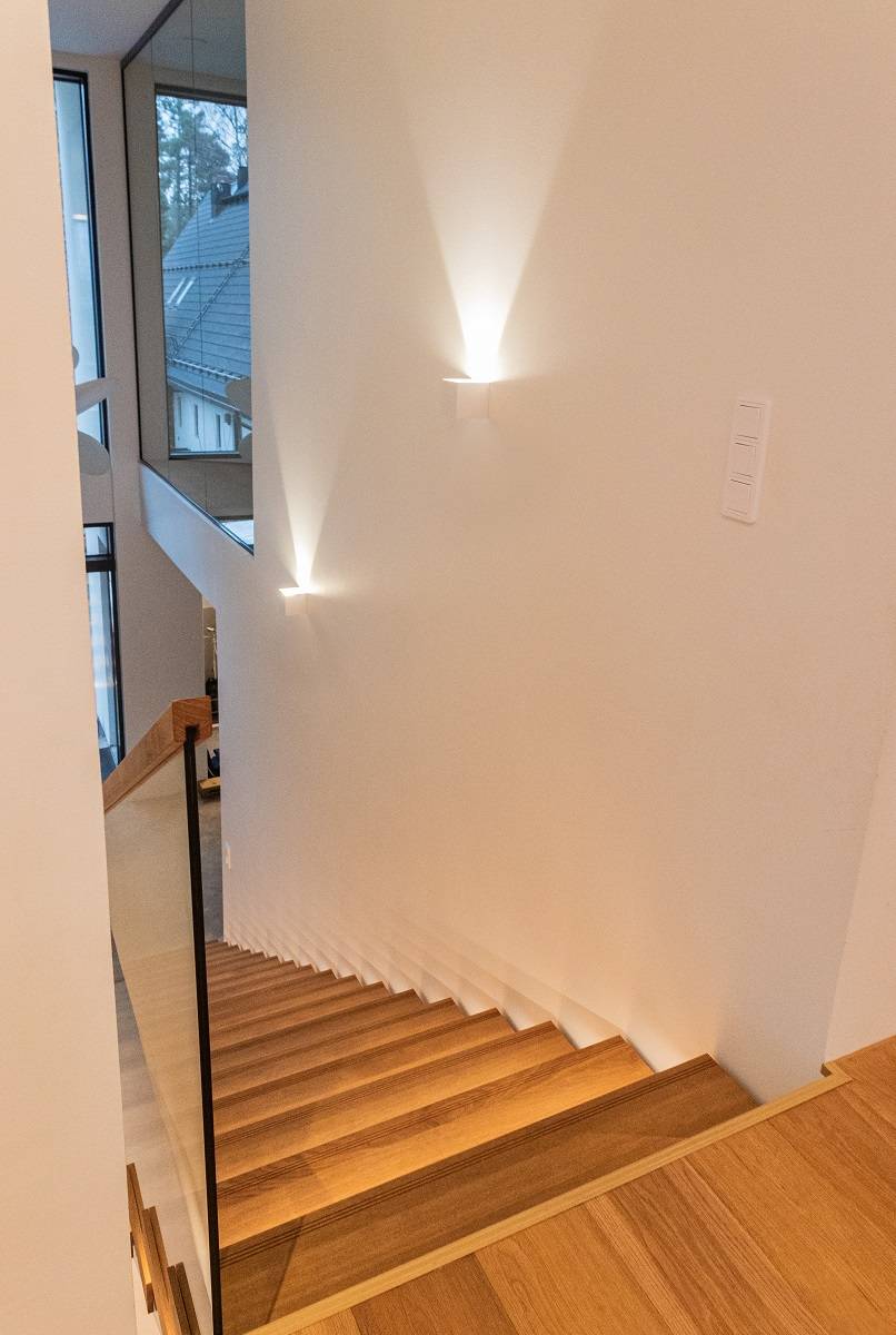 La alta pared blanca de la escalera está iluminada por un nítido foco del aplique FUNKit.